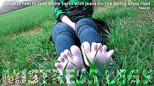 the goddess spreads her cute feet in white socks and jeans on spring grass
