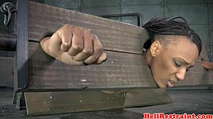 Bound ebony woman restrained in pillory receives discipline
